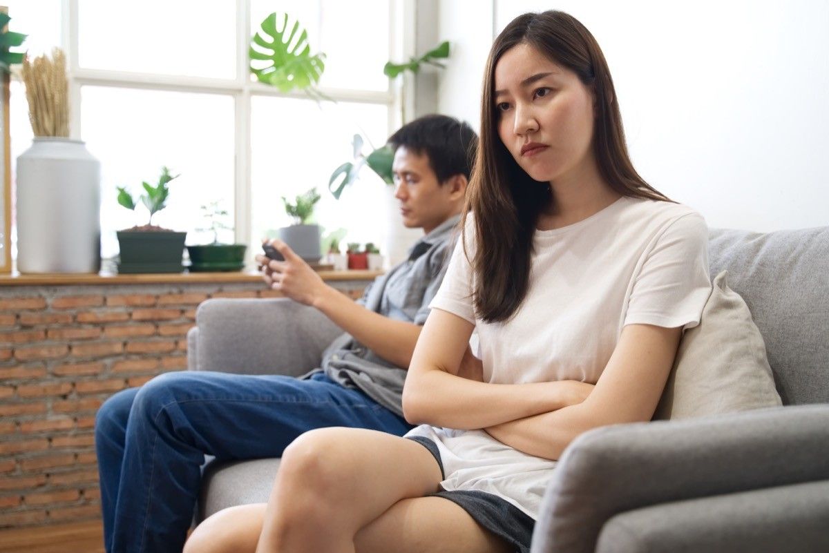 年轻夫妇坐在沙发上,彼此之间,女孩看上去很沮丧,男人在电话上