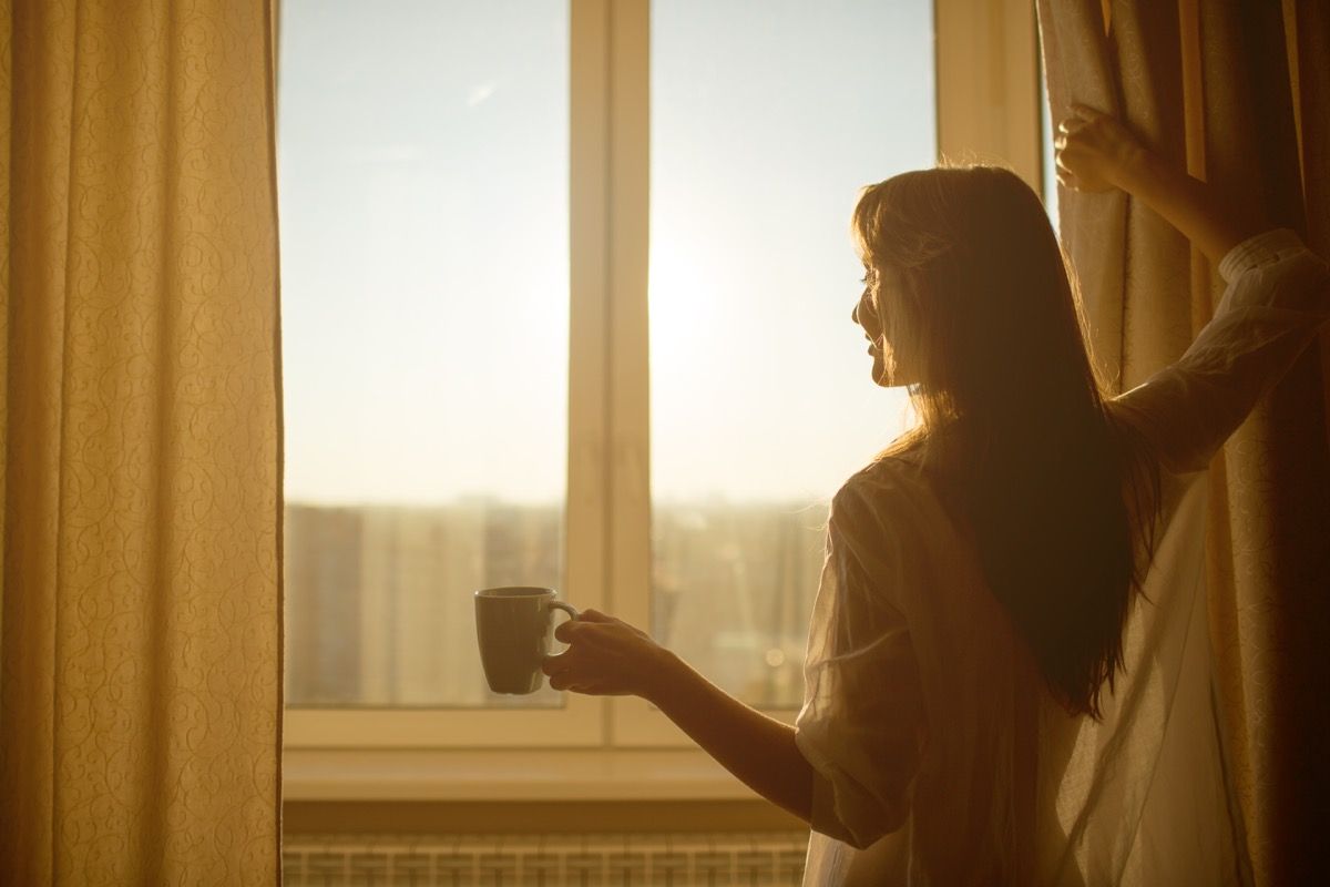 女人在早晨打开窗帘喝咖啡