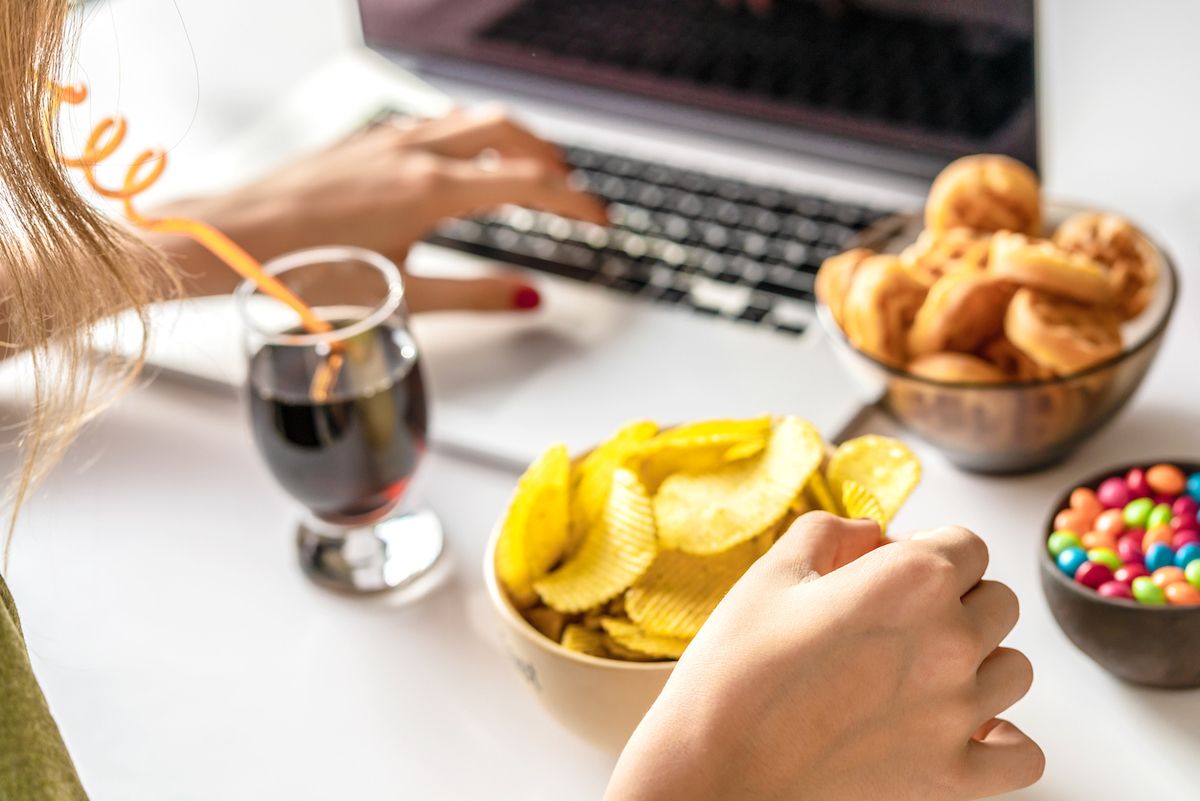 女人在电脑前工作，吃不健康的食物:薯片、饼干、糖果、华夫饼、苏打水