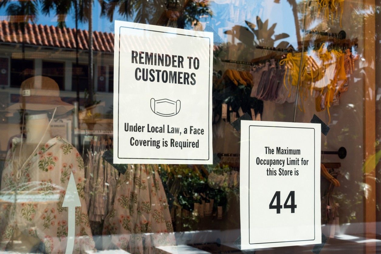 商店橱窗里的两个标志限制了44人的入住率，并要求戴口罩。
